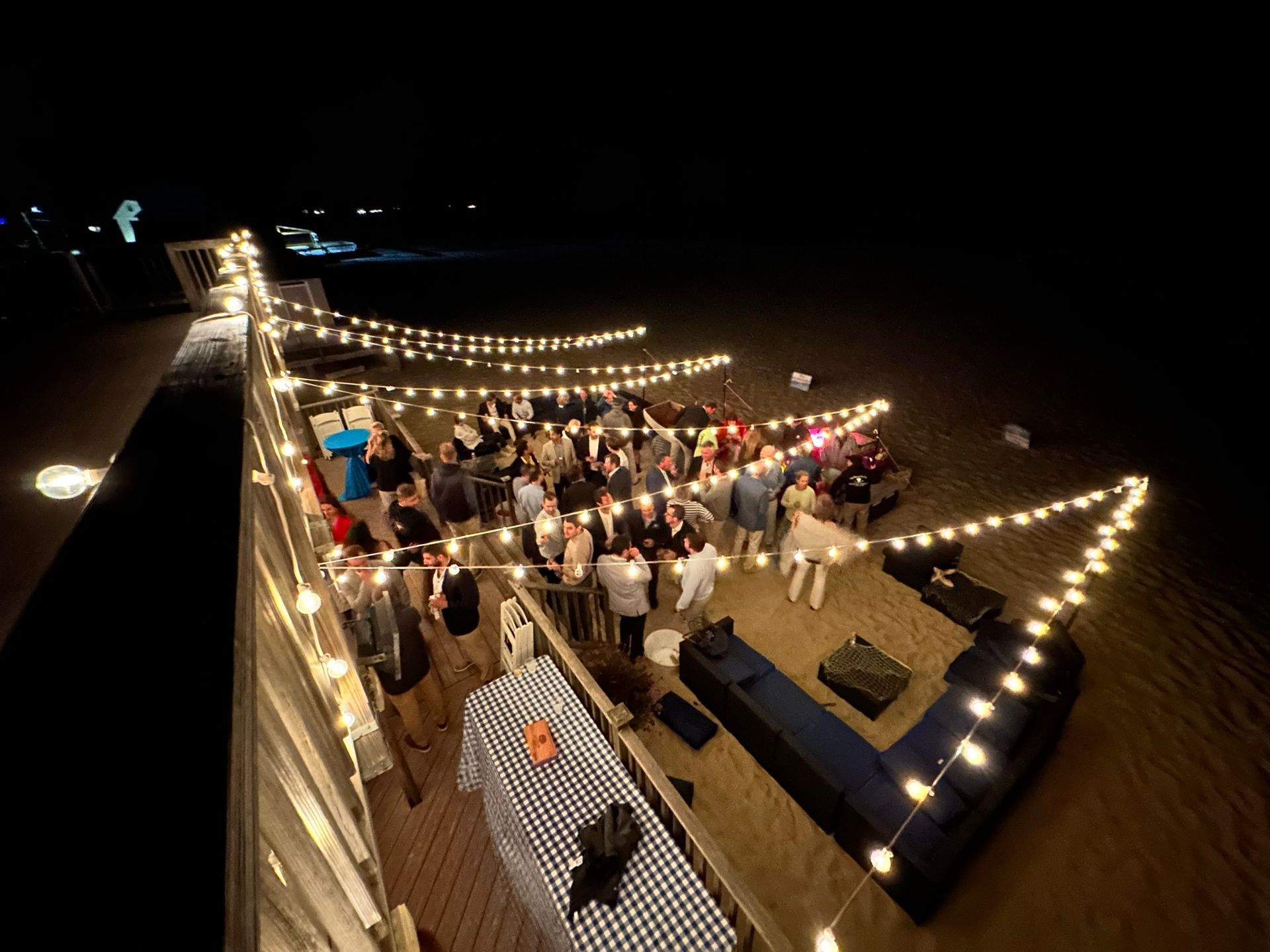 Outdoor night event on a pier, with string lights and people socializing.