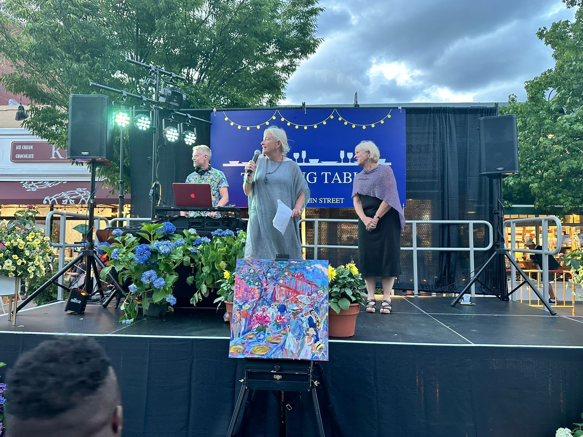 People on stage with artwork; flowers, lights, and buildings in the background.