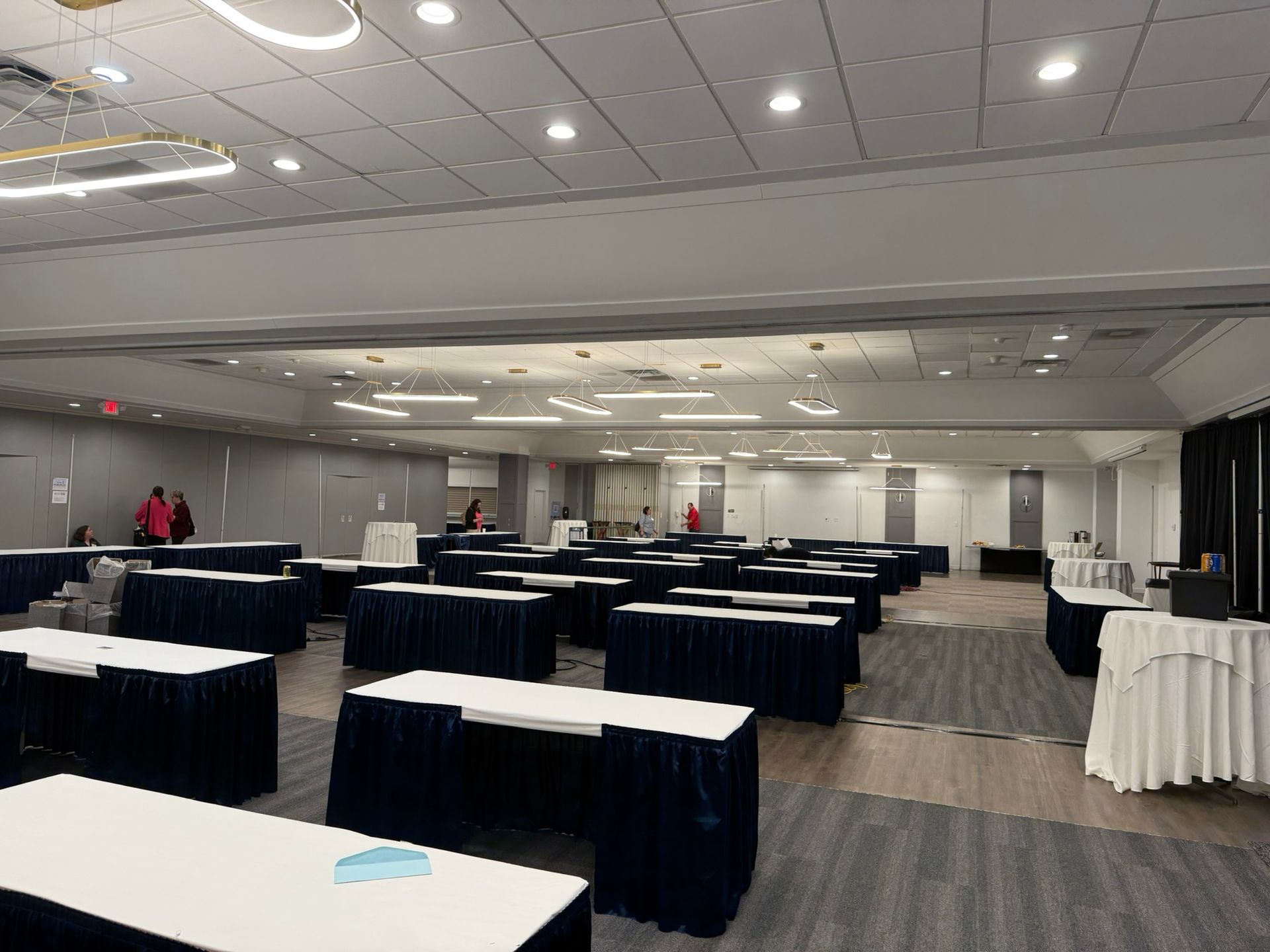 Empty conference room with rows of tables, covered in blue and white linens, ready for a meeting.