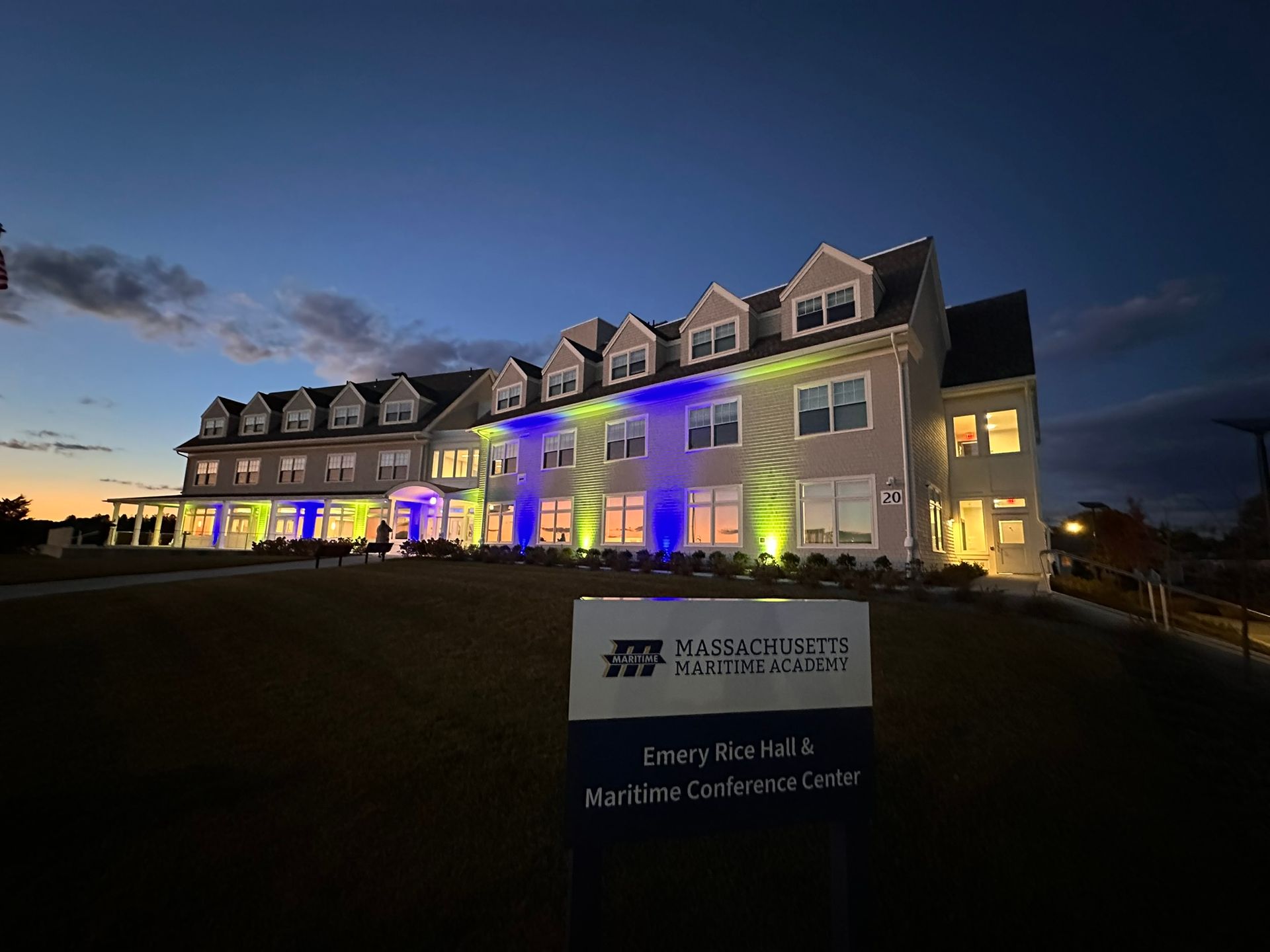 Building facade lit with blue and green lights at dusk. Sign reads 
