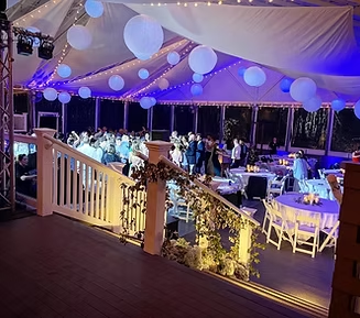 Party tent with people dancing and eating at tables, blue and white lighting, and string lights.