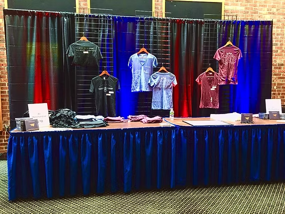 Clothing display table with shirts, black and blue curtain backdrop.