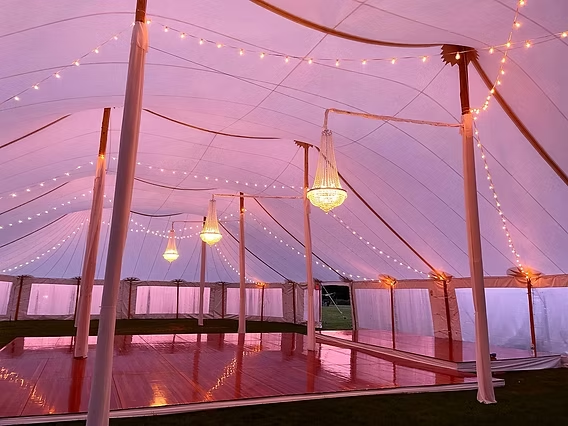 Inside a white tent with string lights and chandeliers; wooden dance floor.