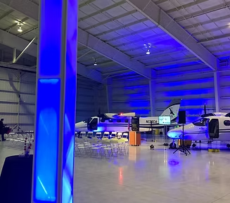 Blue-lit event in a hangar with two small planes, tables, and lighting setup.