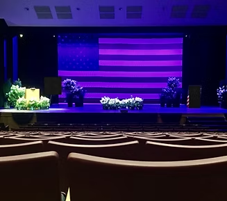 Auditorium stage with projected purple American flag, flowers, and seating.