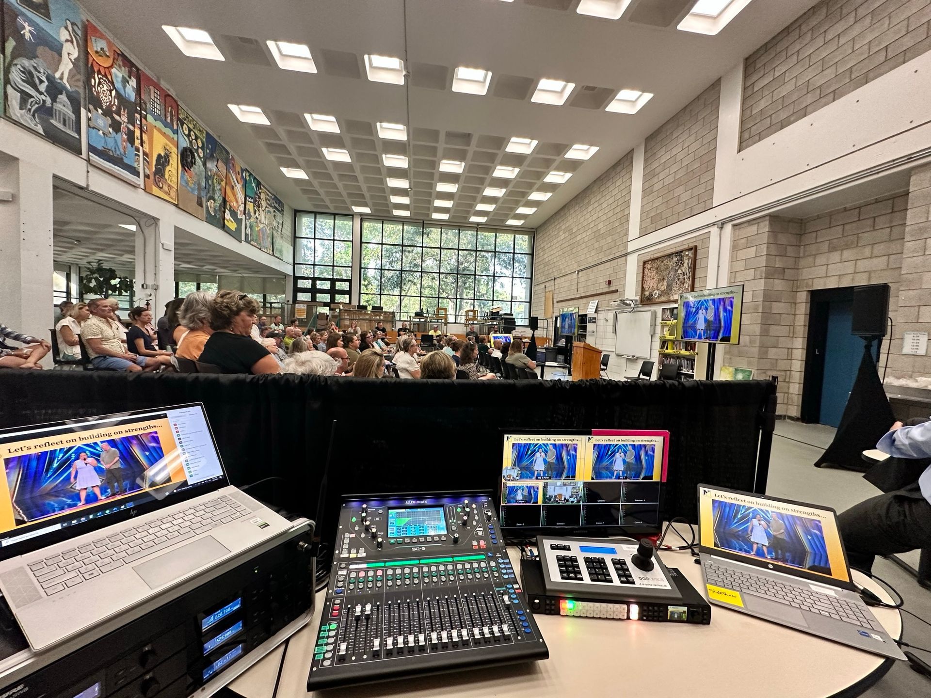 A conference room with an audience. Video and audio equipment is set up in front.