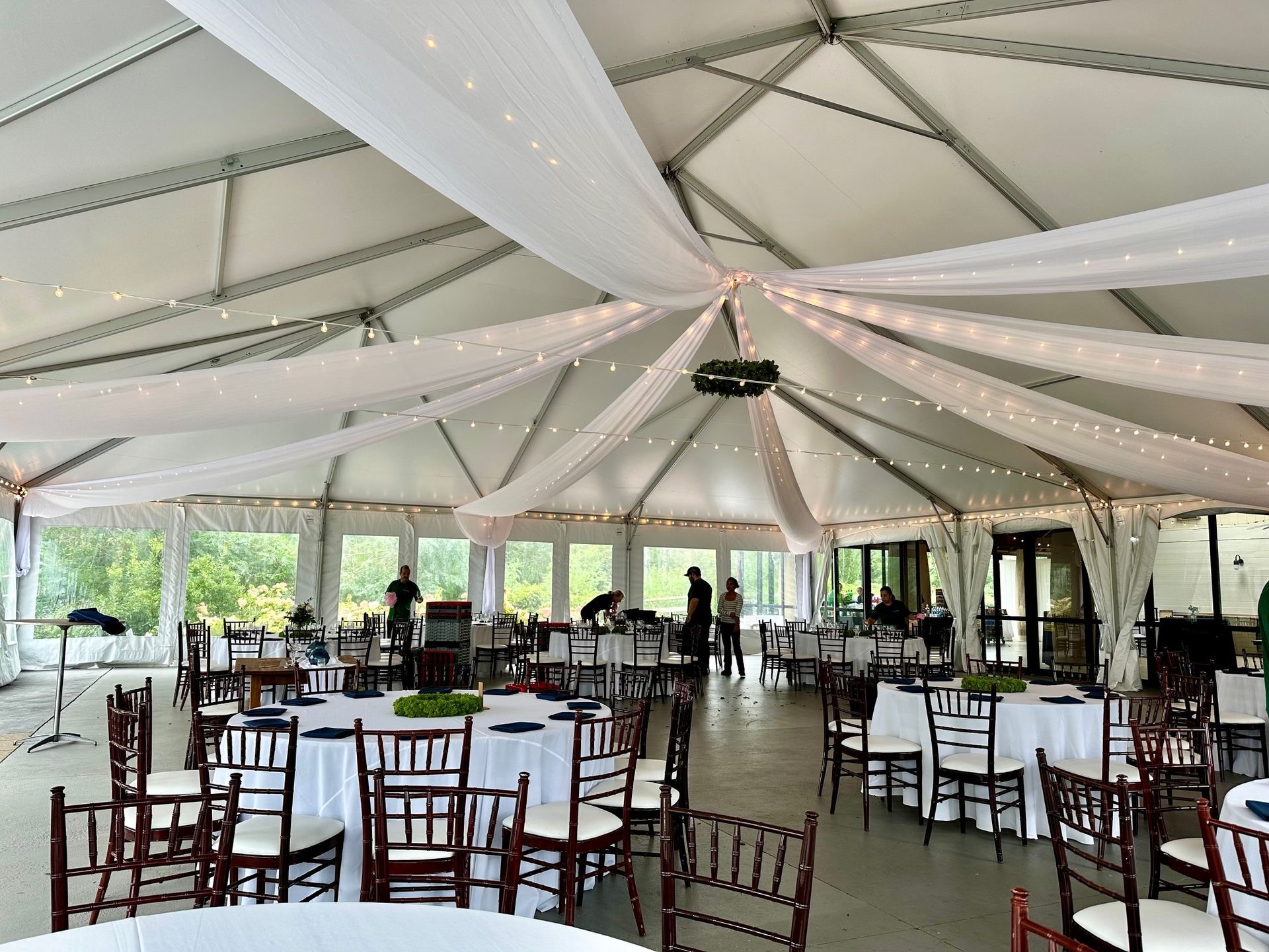 Indoor event tent decorated with white fabric, string lights, tables, and chairs.