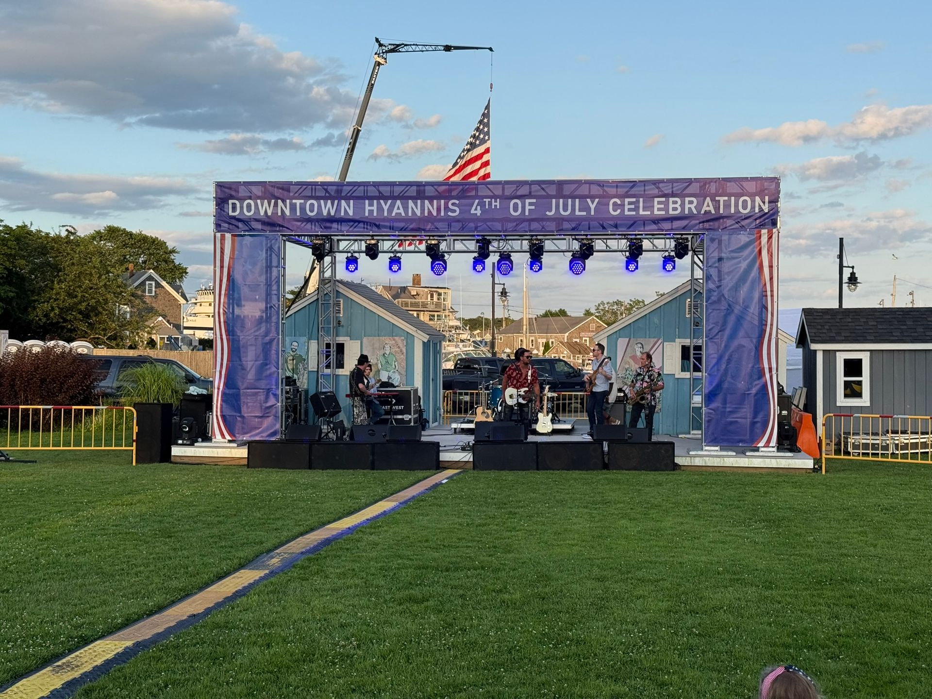 Band performing on stage at a Fourth of July celebration in Hyannis, Massachusetts, with American flag and blue stage decorations.