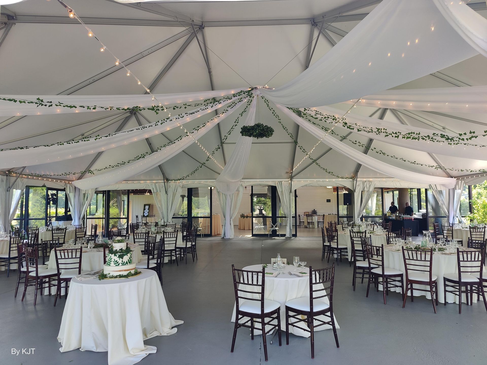 Wedding reception inside a white tent with draped fabric, fairy lights, tables, and chairs.