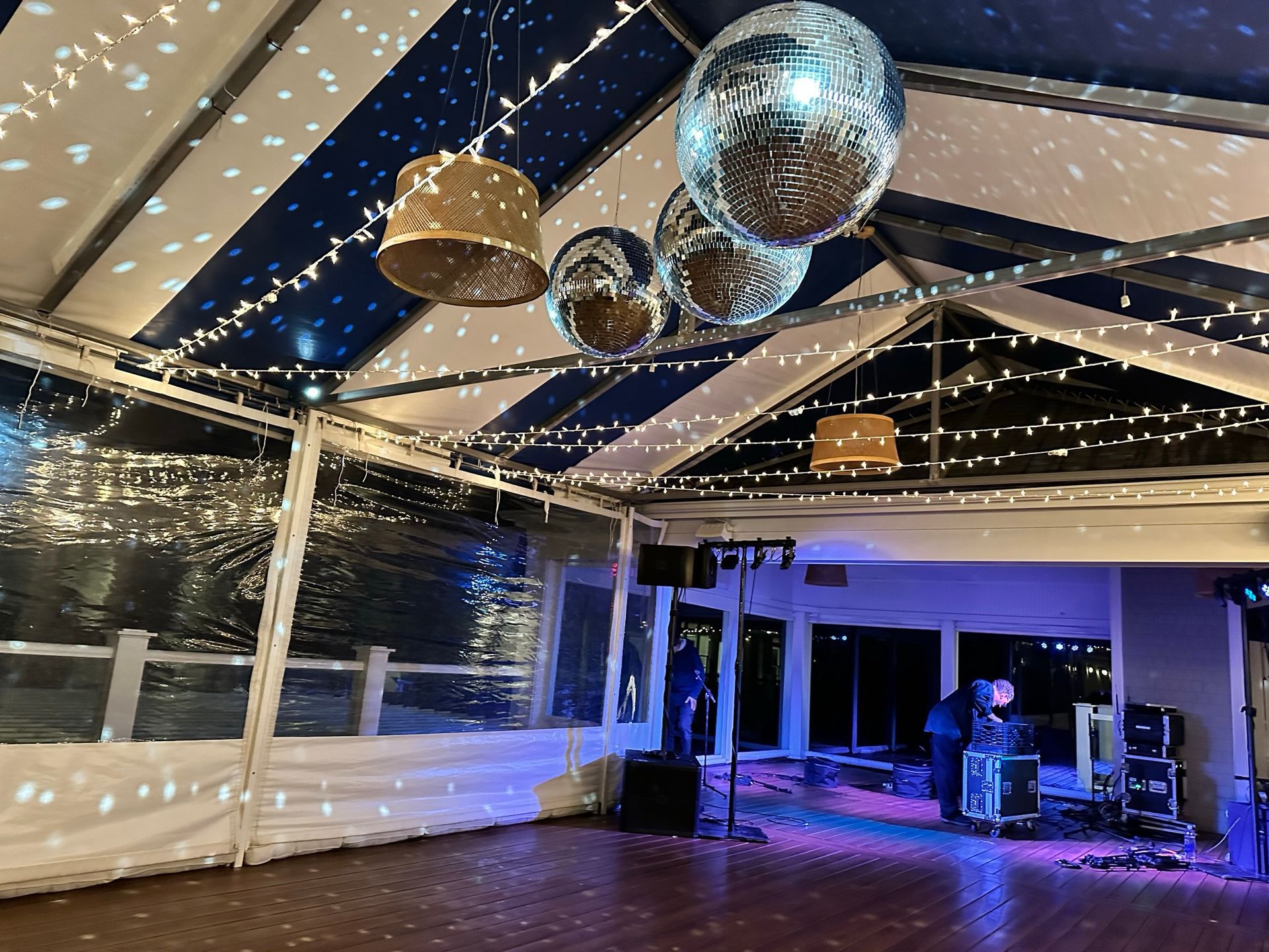 Party tent interior with disco balls, string lights, and a band setup. Blue and white striped ceiling.
