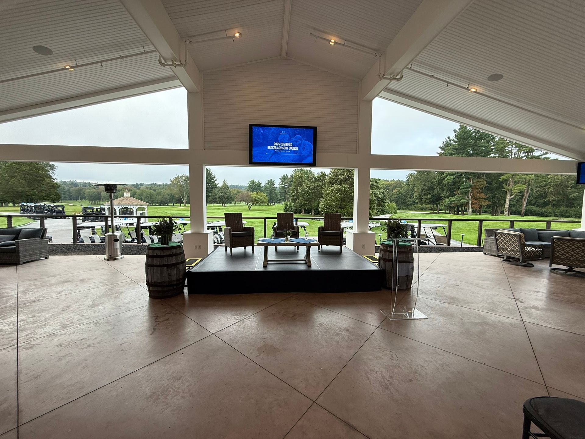 A paneled room overlooking a golf course. Stage with chairs faces a TV. Outside is a green course.