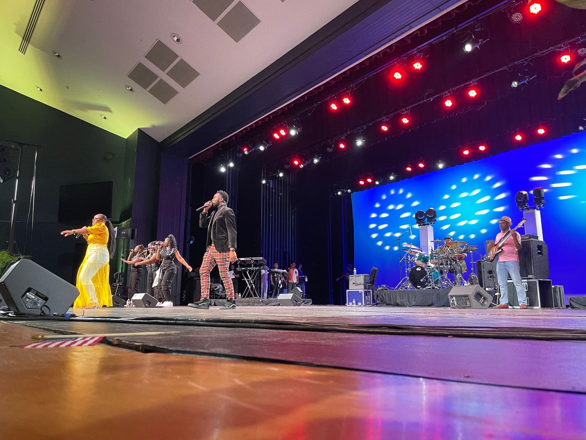 Band performing on stage with dancers; blue backdrop, stage lights, and audience seating.