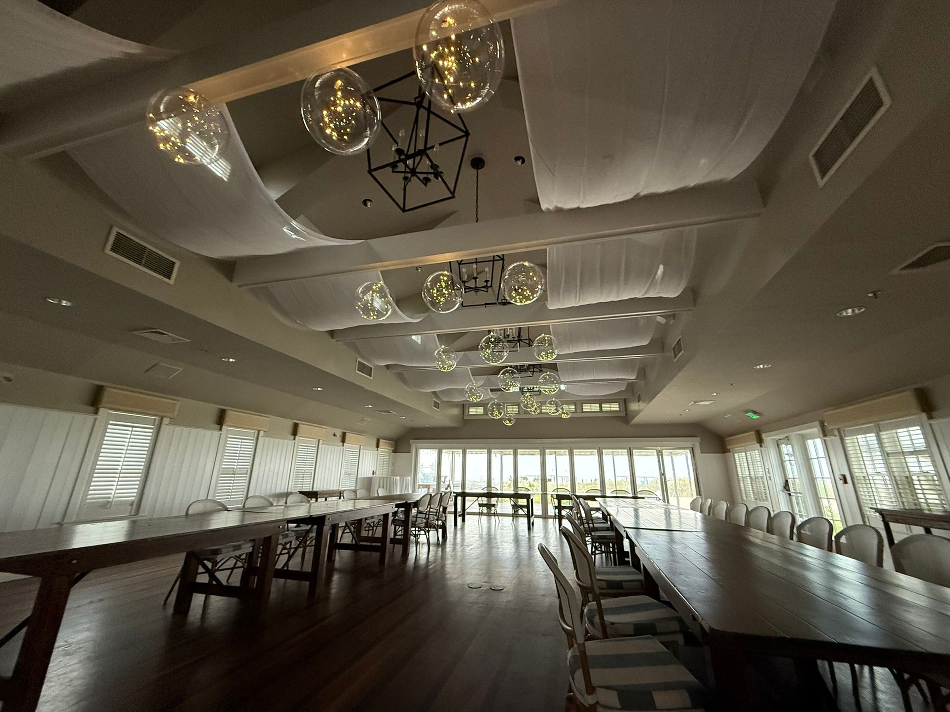 Long wooden tables with chairs in a bright room with hanging lights and fabric.
