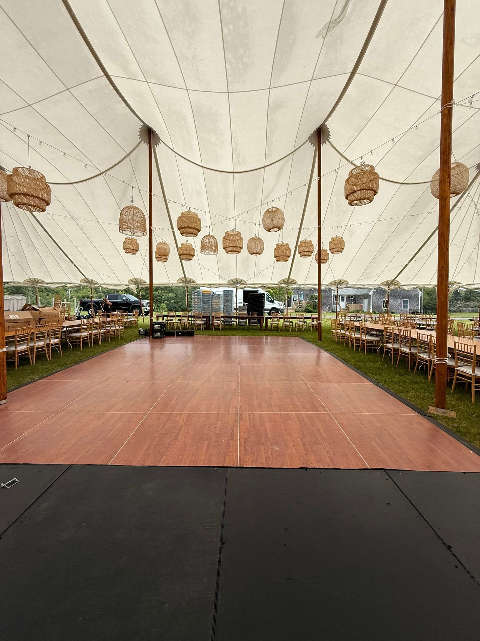 Event tent with wood dance floor, tables, and hanging lanterns.