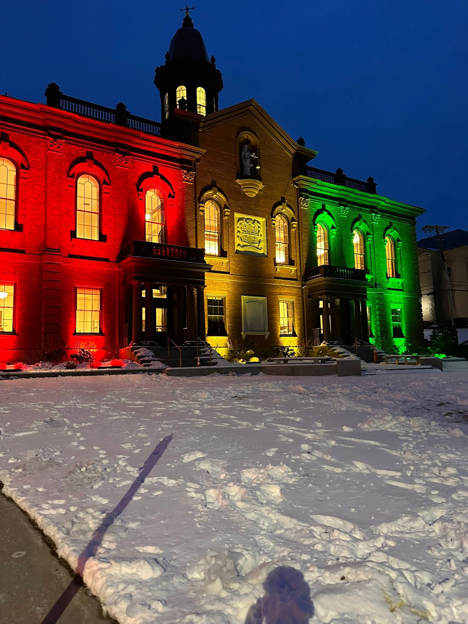 A building lit in red, gold, and green stands in the snow at night.
