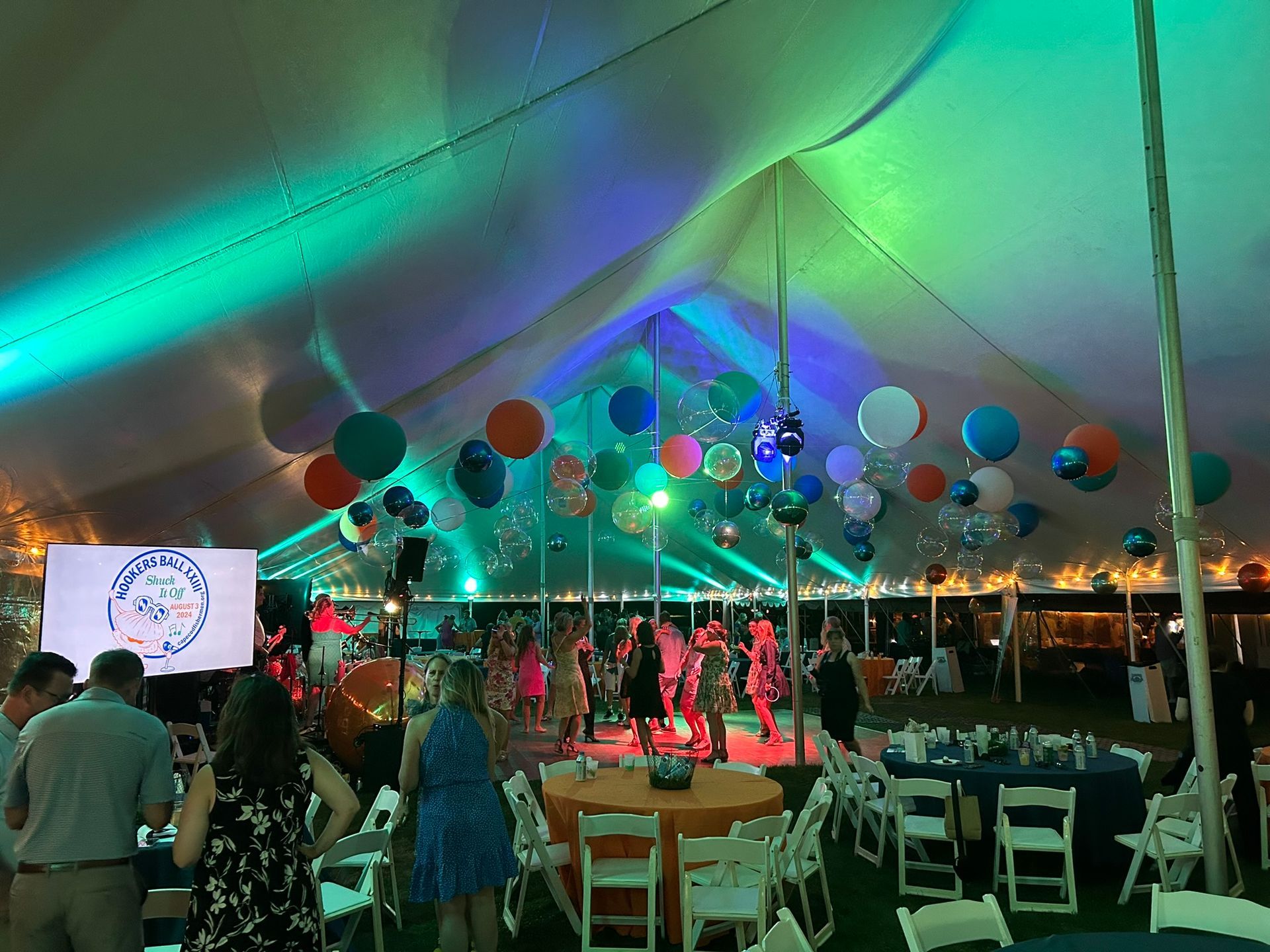 Party tent with people dancing and balloons under colorful lights.