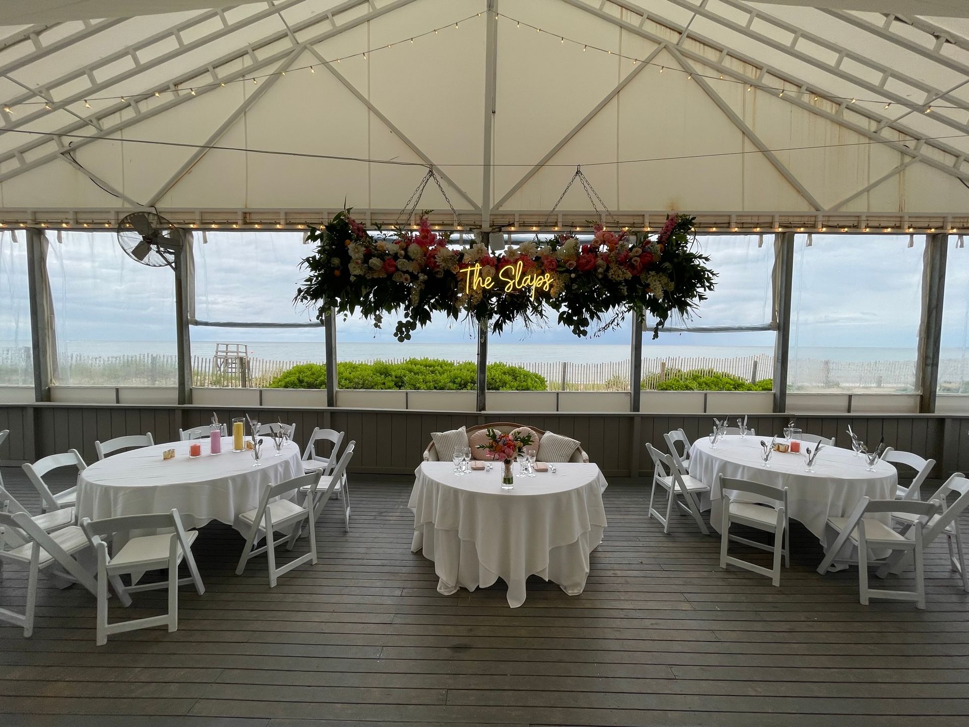 Wedding reception area with tables, chairs, and floral decor overlooking the ocean.