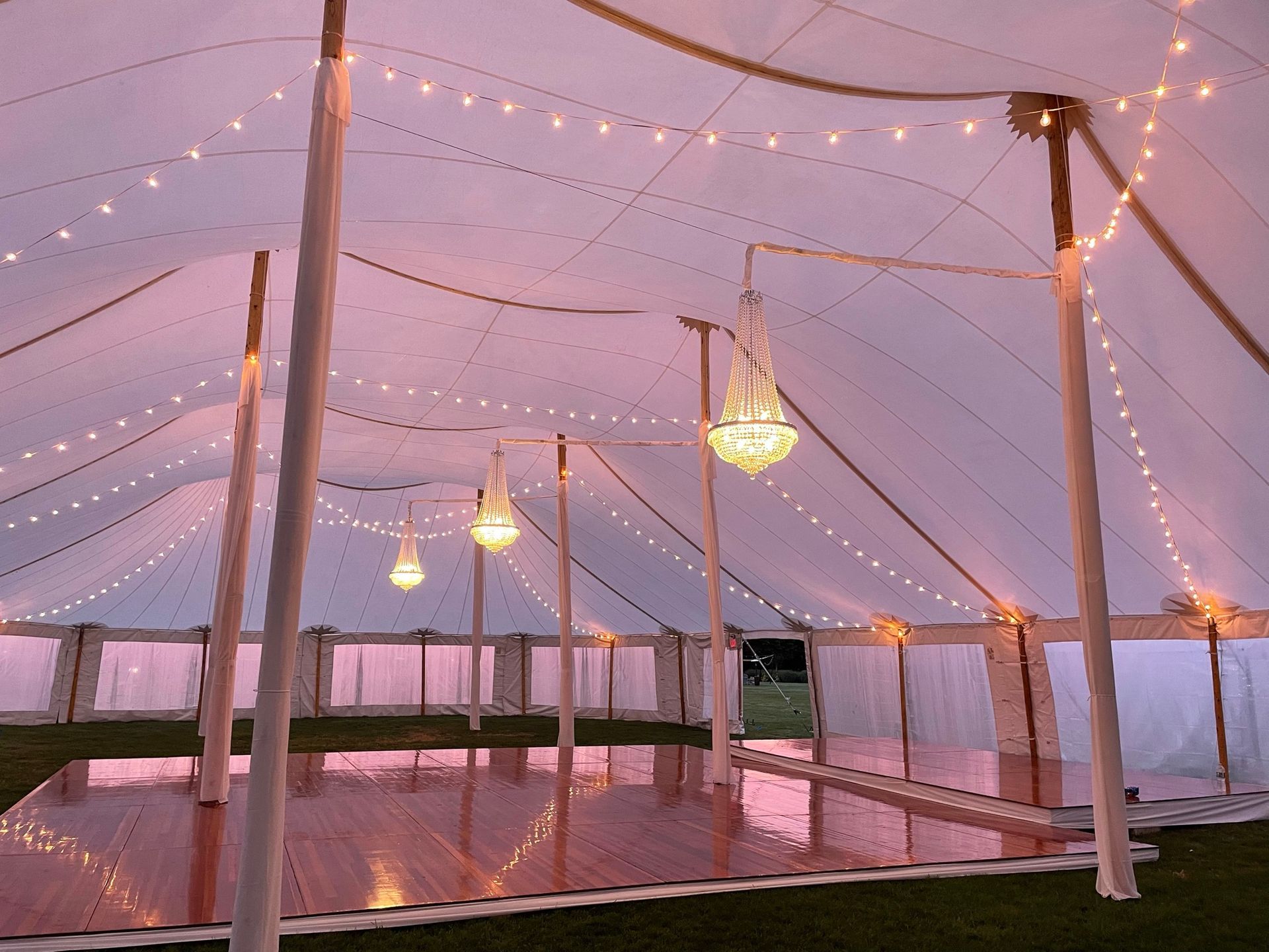Inside a white tent decorated with string lights and chandeliers; wooden dance floor.