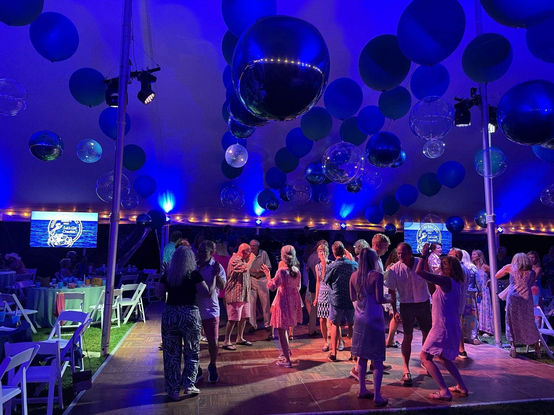 Party tent with dancing people and blue balloons, disco balls, and spotlights.