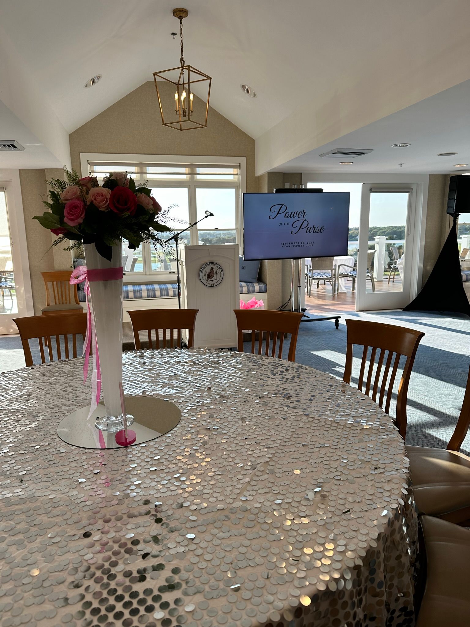 A round table set for a formal event, featuring a large flower arrangement, with a screen and chairs.