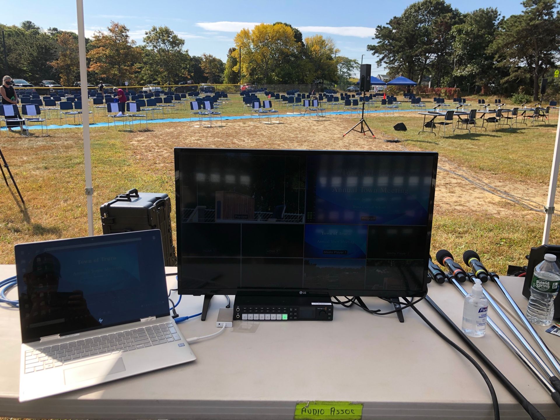 Laptop and monitor on table, overlooking an outdoor sporting event setup with targets and chairs.