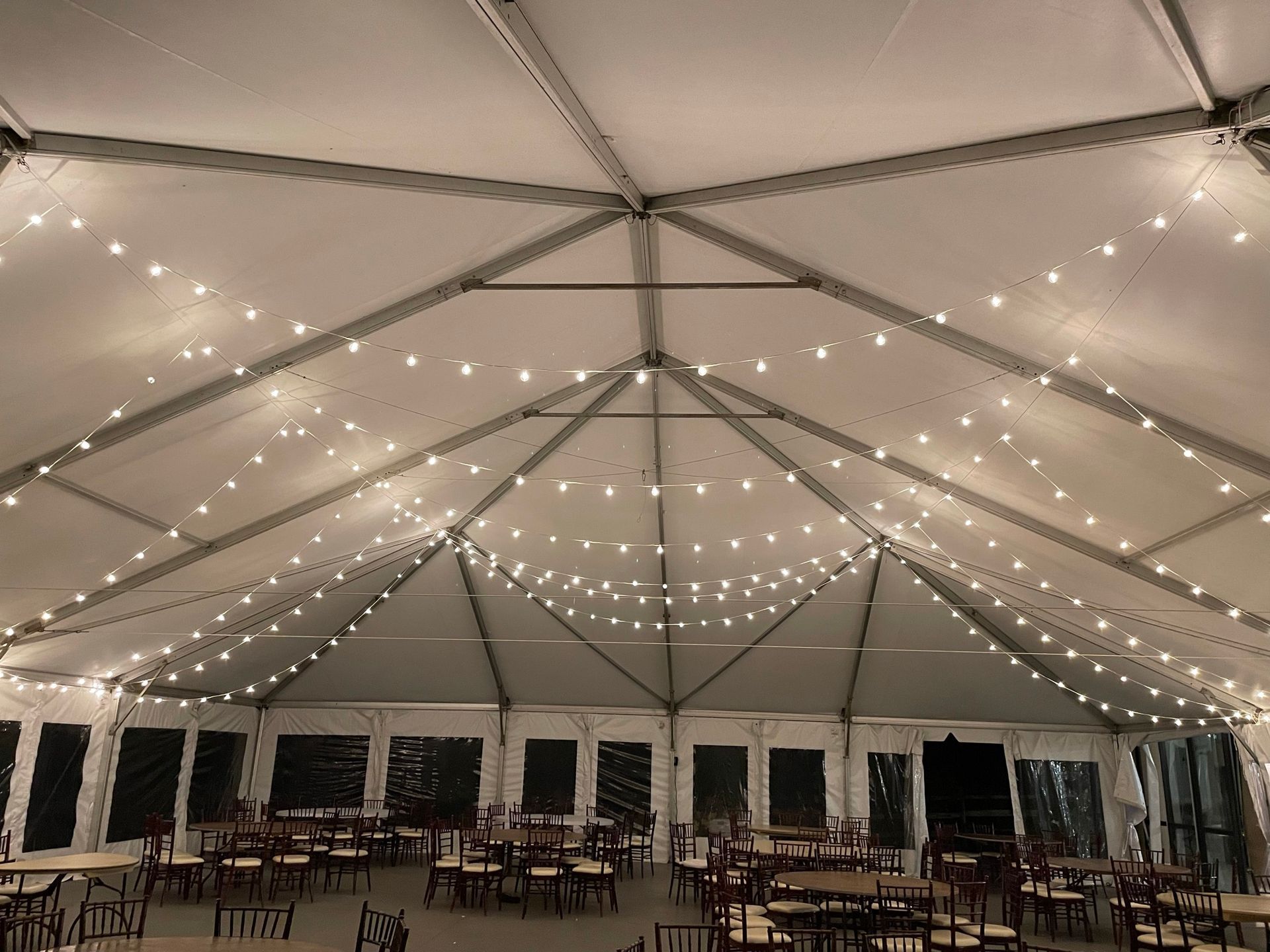 Tent interior with string lights, tables, and chairs set up for an event.