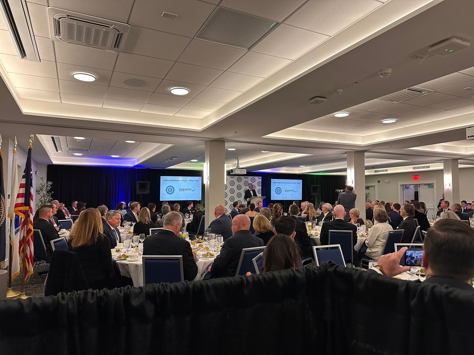 A large, well-lit banquet hall with many people seated at tables, likely attending an event.