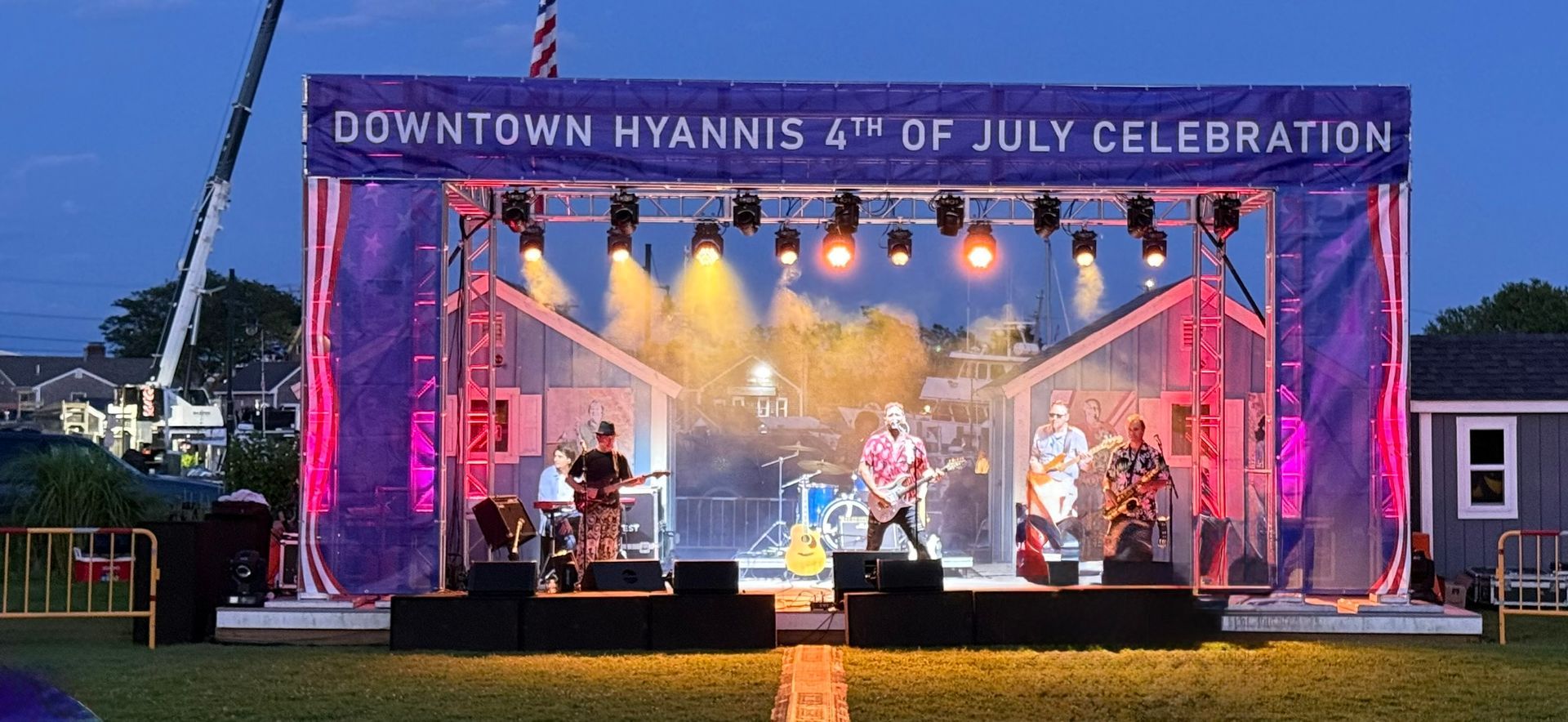 Band performing on stage at a Downtown Hyannis 4th of July Celebration. Stage lit up with red, blue, and yellow lights.