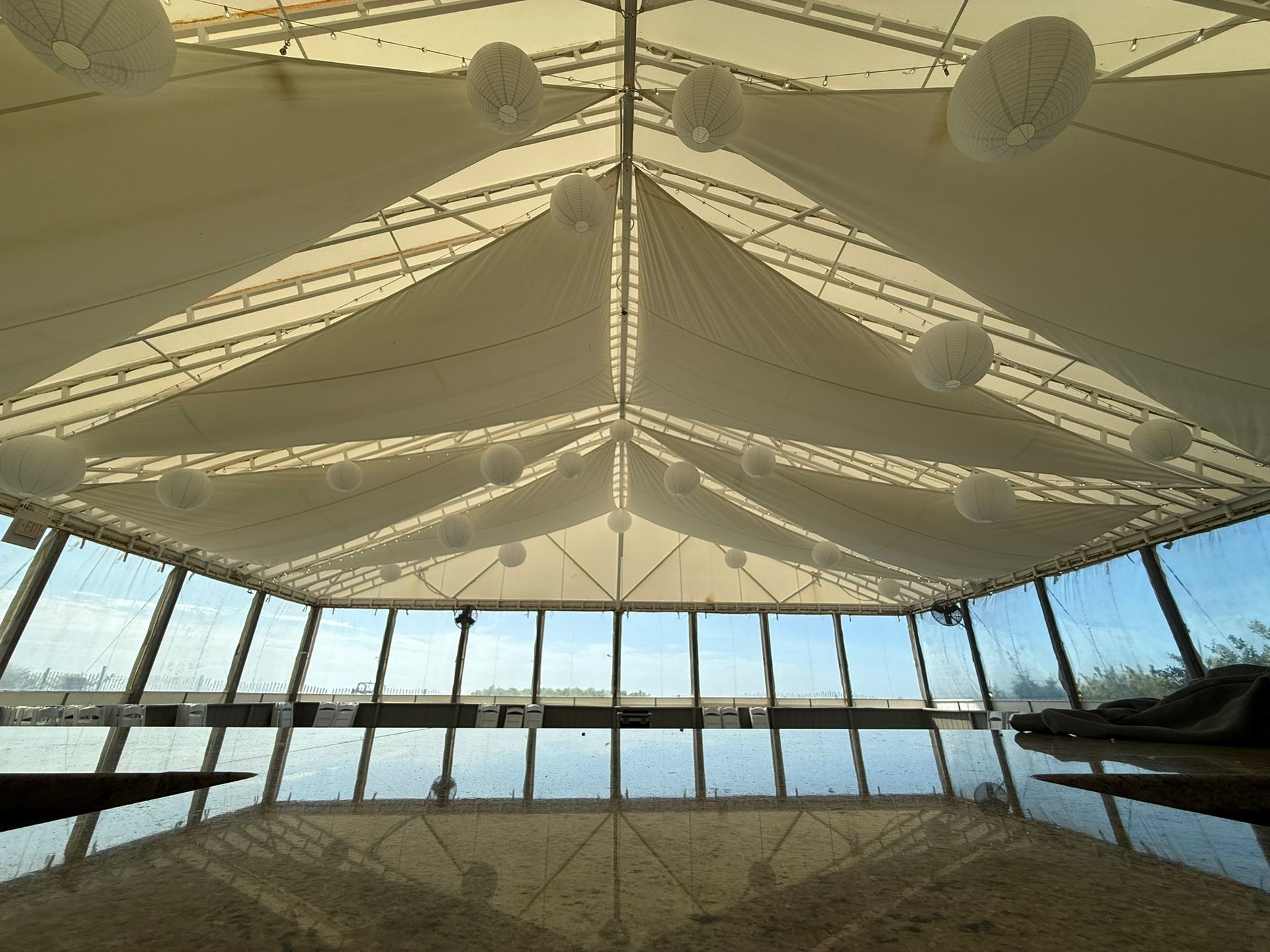 Inside a tent-like structure with a white ceiling and large windows reflecting the outside. Round lights hang from the ceiling.