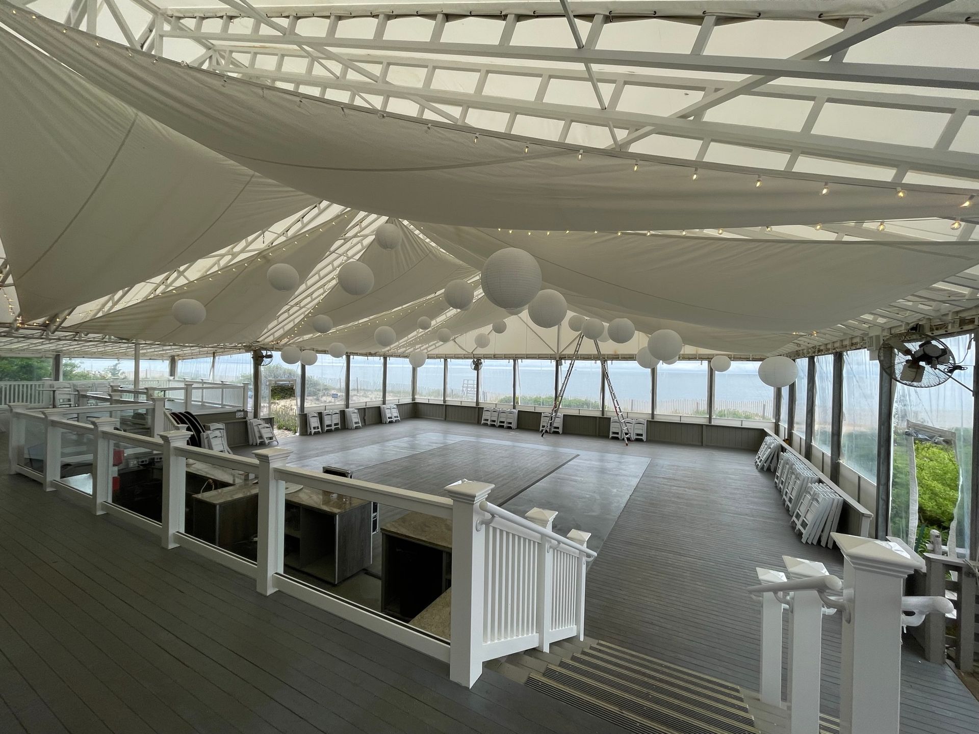 Outdoor event space with white canopy, string lights, and dance floor overlooking water.