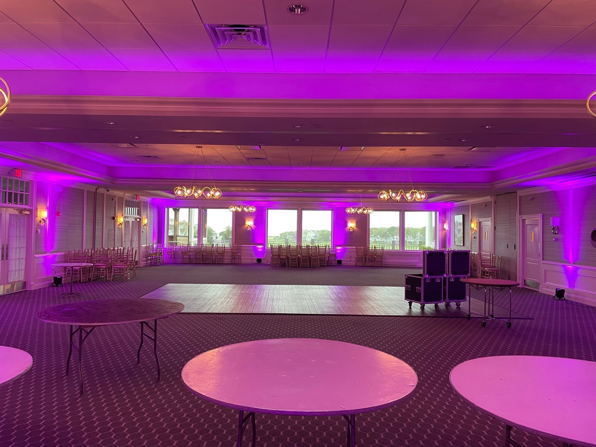 Empty banquet hall with round tables and a dance floor, lit with purple uplighting.