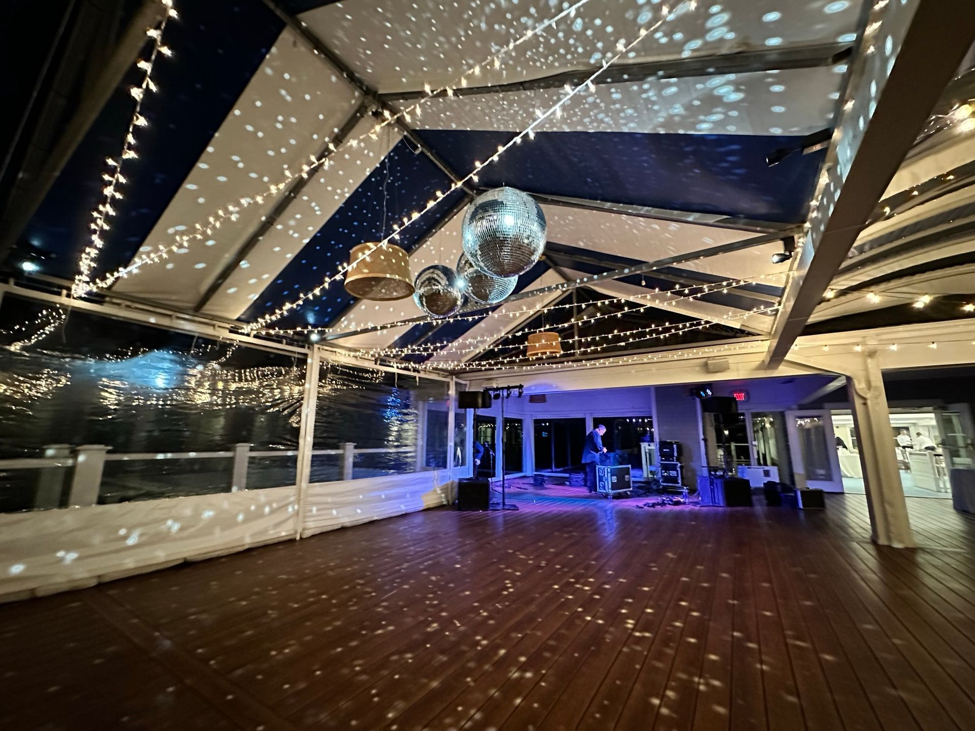 An open-air dance floor with a band, disco balls, string lights, and a striped ceiling.