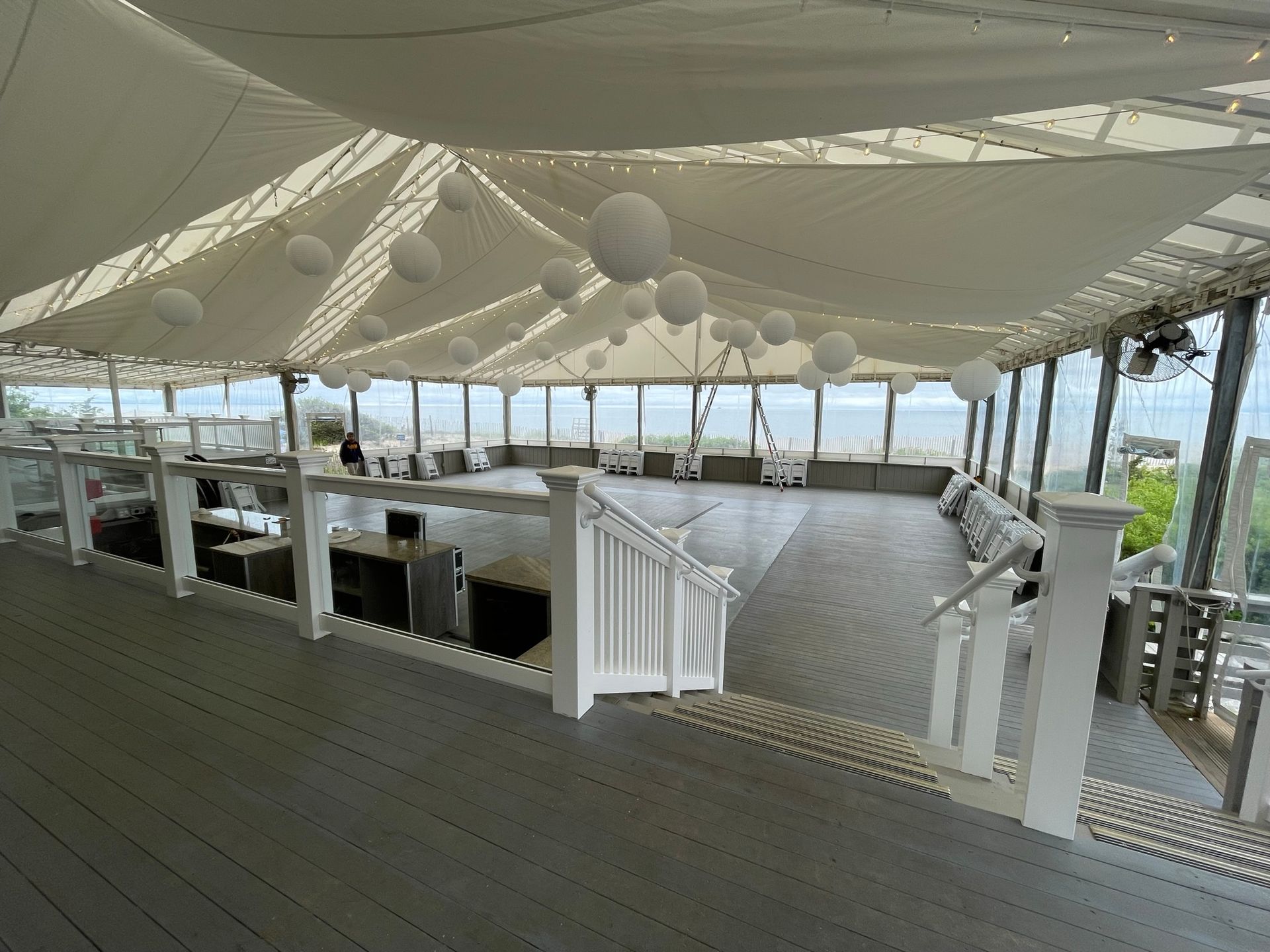 Decked outdoor event space with white tent ceiling, string lights, and ocean views.