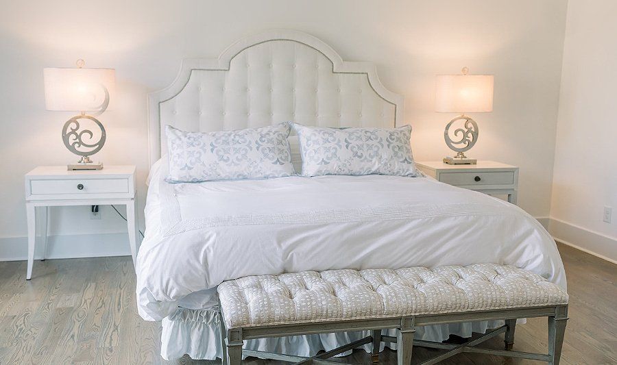 A bedroom with a bed , nightstands , lamps and a bench.