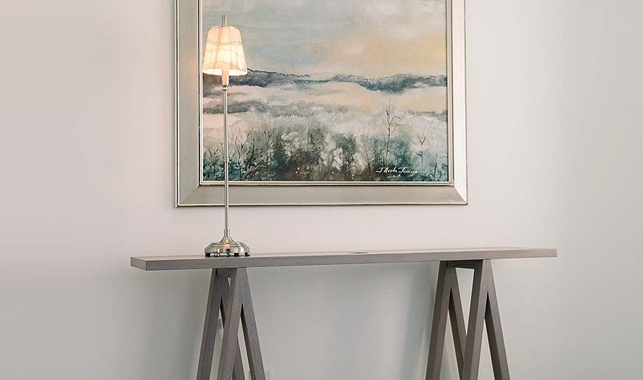 A table with a lamp and a painting on the wall above it.