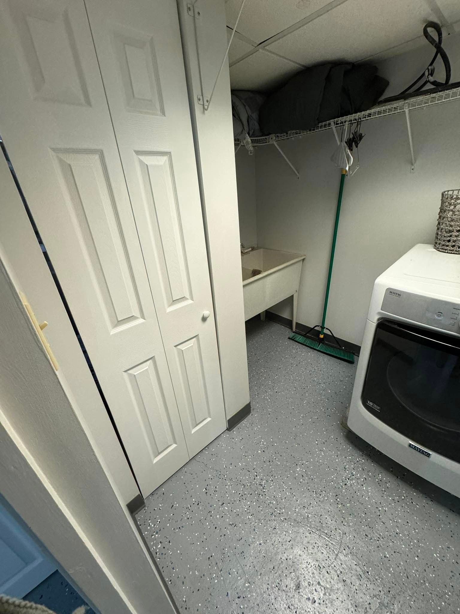 Laundry room with white bi-fold doors, sink, washer, and speckled gray floor.