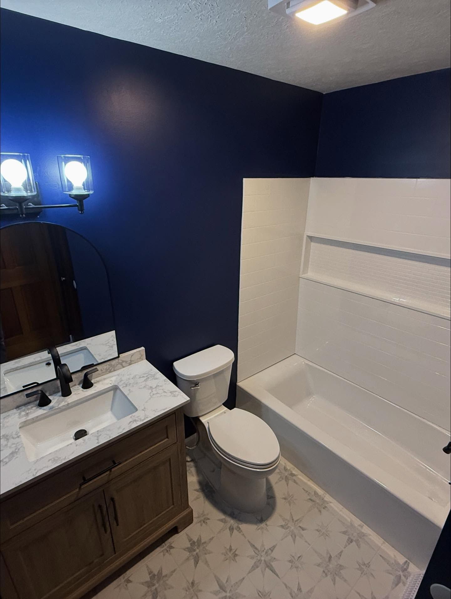 Bathroom with blue walls, white bathtub and toilet, wooden vanity, and patterned floor.