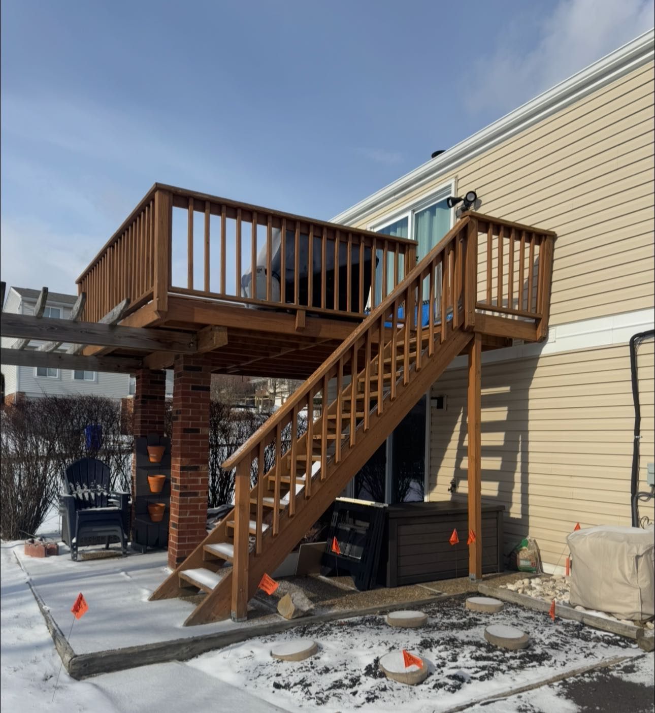 Wooden deck with stairs attached to a beige house, snow on ground.