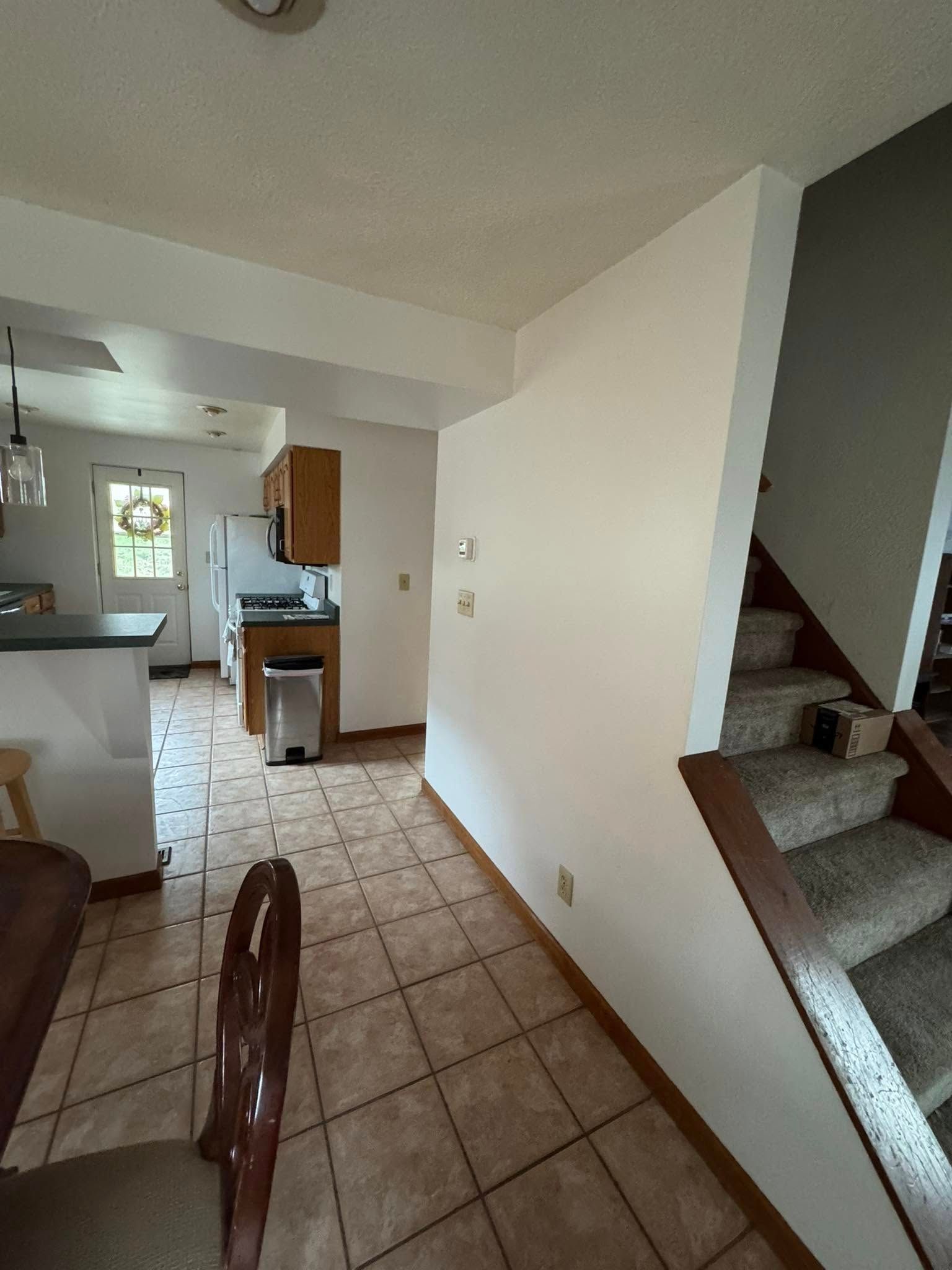 Entryway with staircase and kitchen visible. Beige tile floor, white and brown walls, and wooden cabinets.