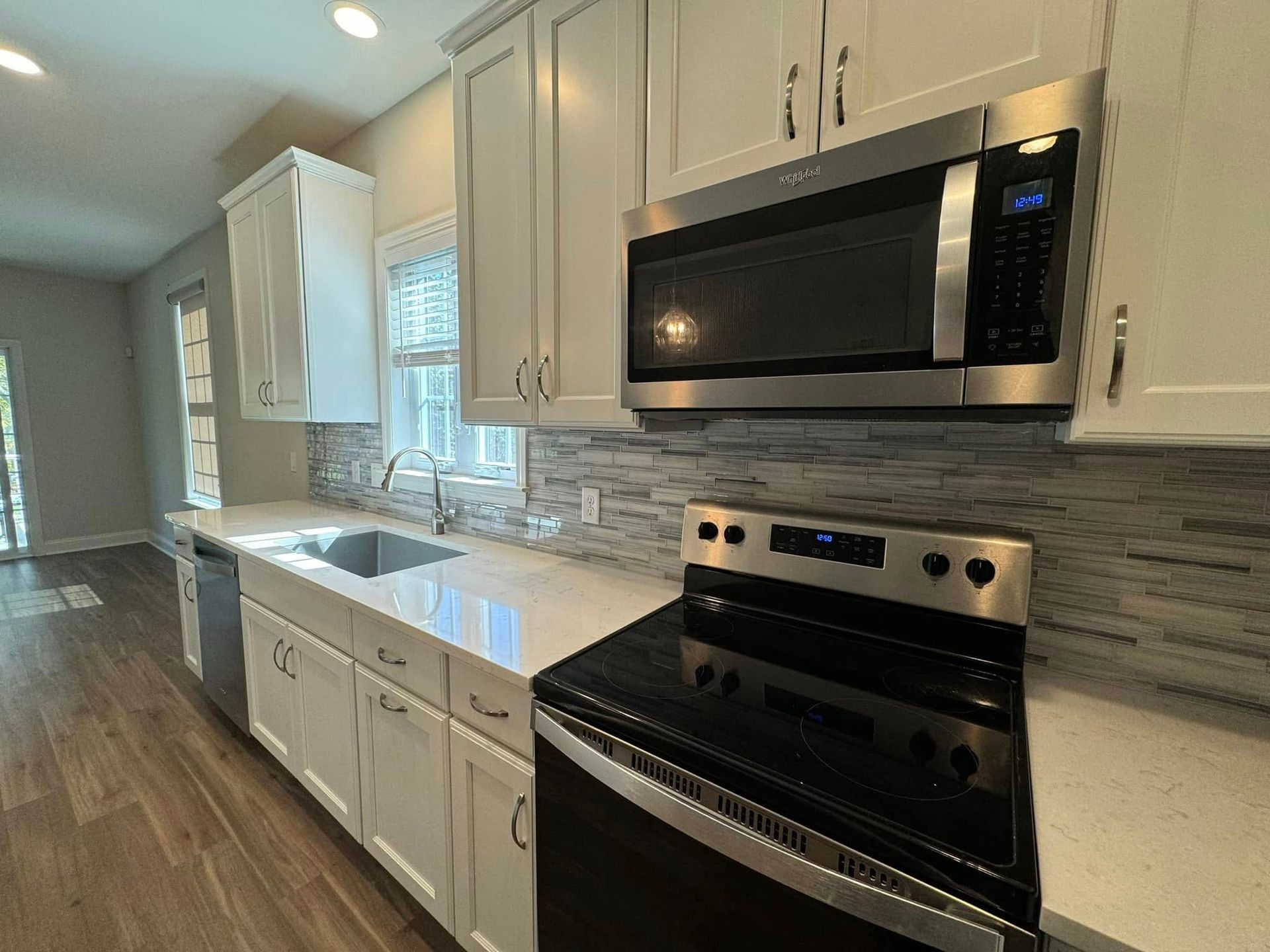 Modern kitchen with white cabinets, stainless steel appliances, and gray tile backsplash.