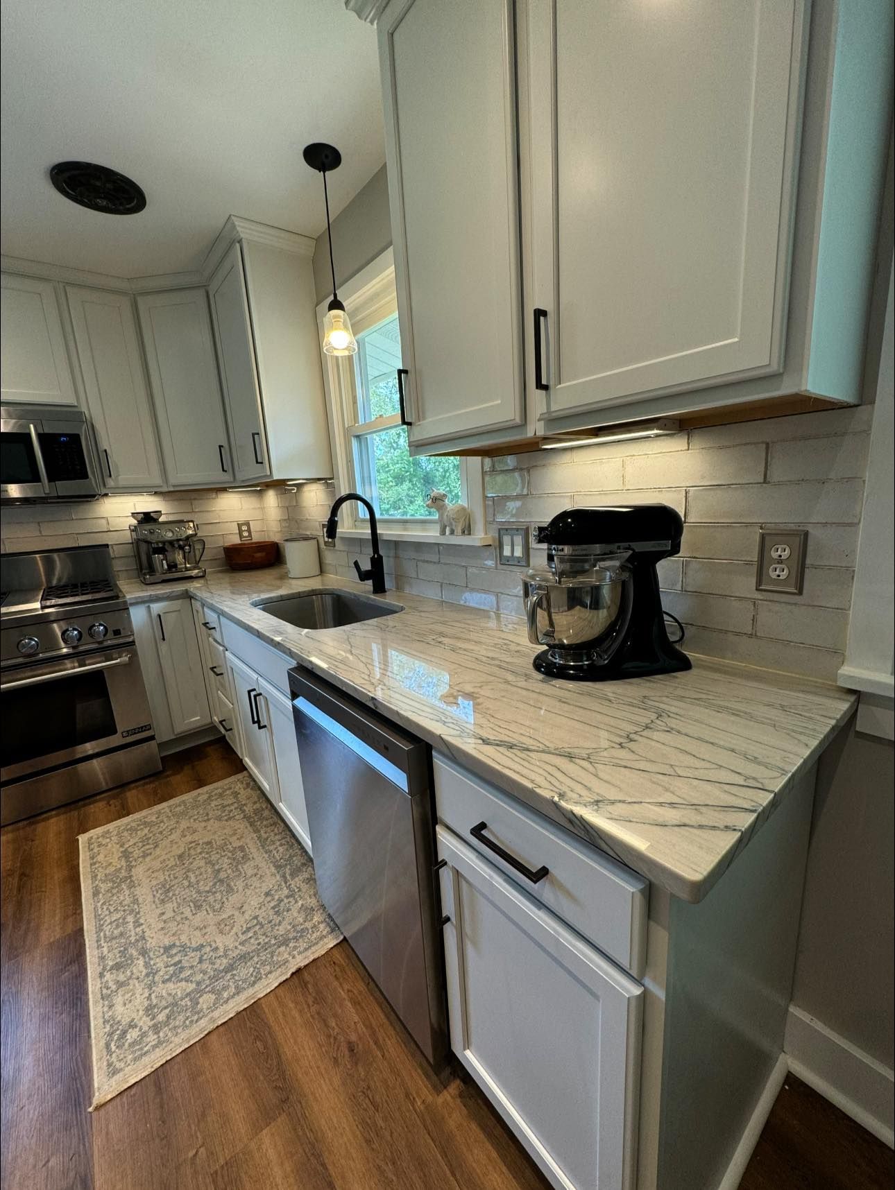 White kitchen with stainless steel appliances, a black mixer, and granite countertops.