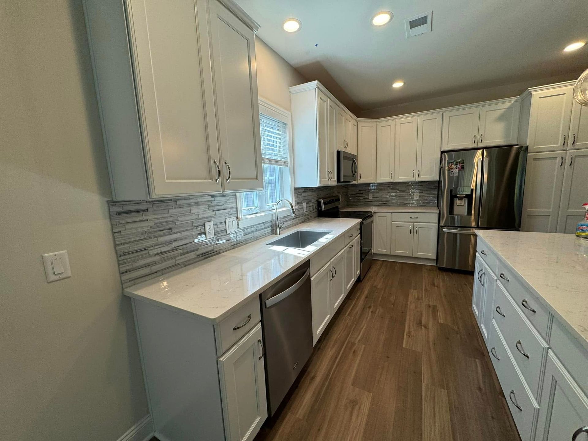 White kitchen with stainless steel appliances, white countertops, and wood-look flooring.