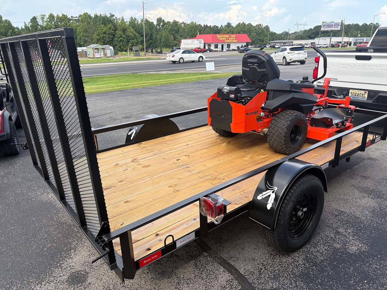 Orange riding mower on a black utility trailer at a roadside parking lot
