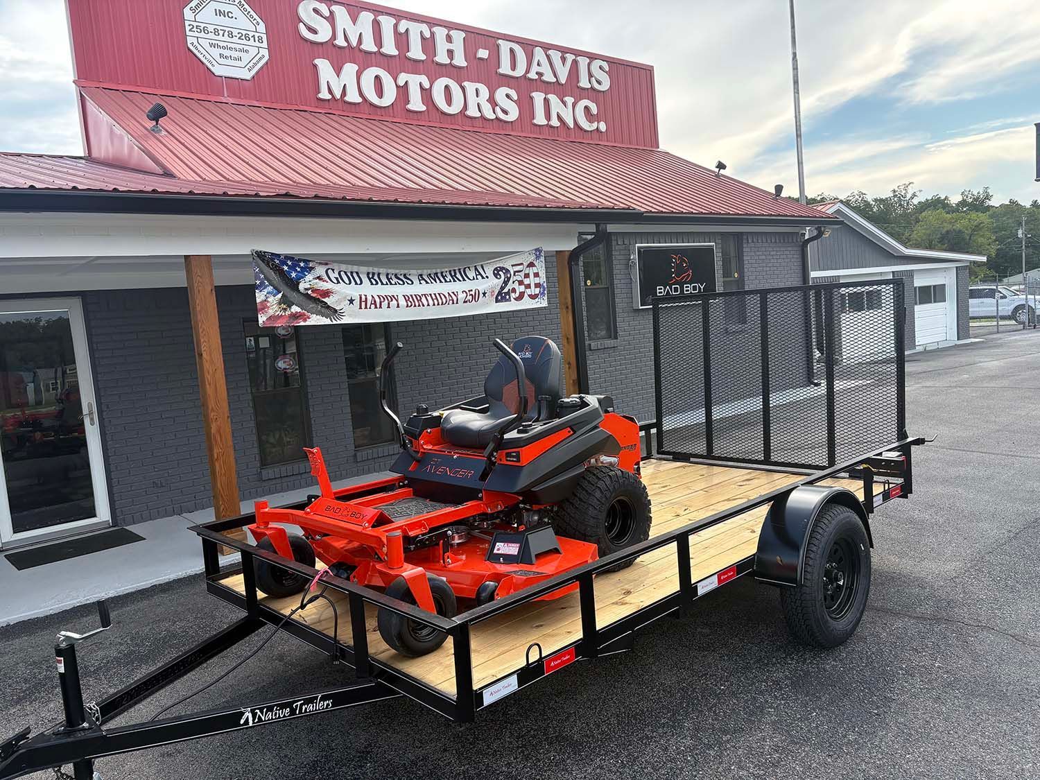 Orange riding lawn mower on a black flatbed trailer outside Smith-Davis Motors Inc