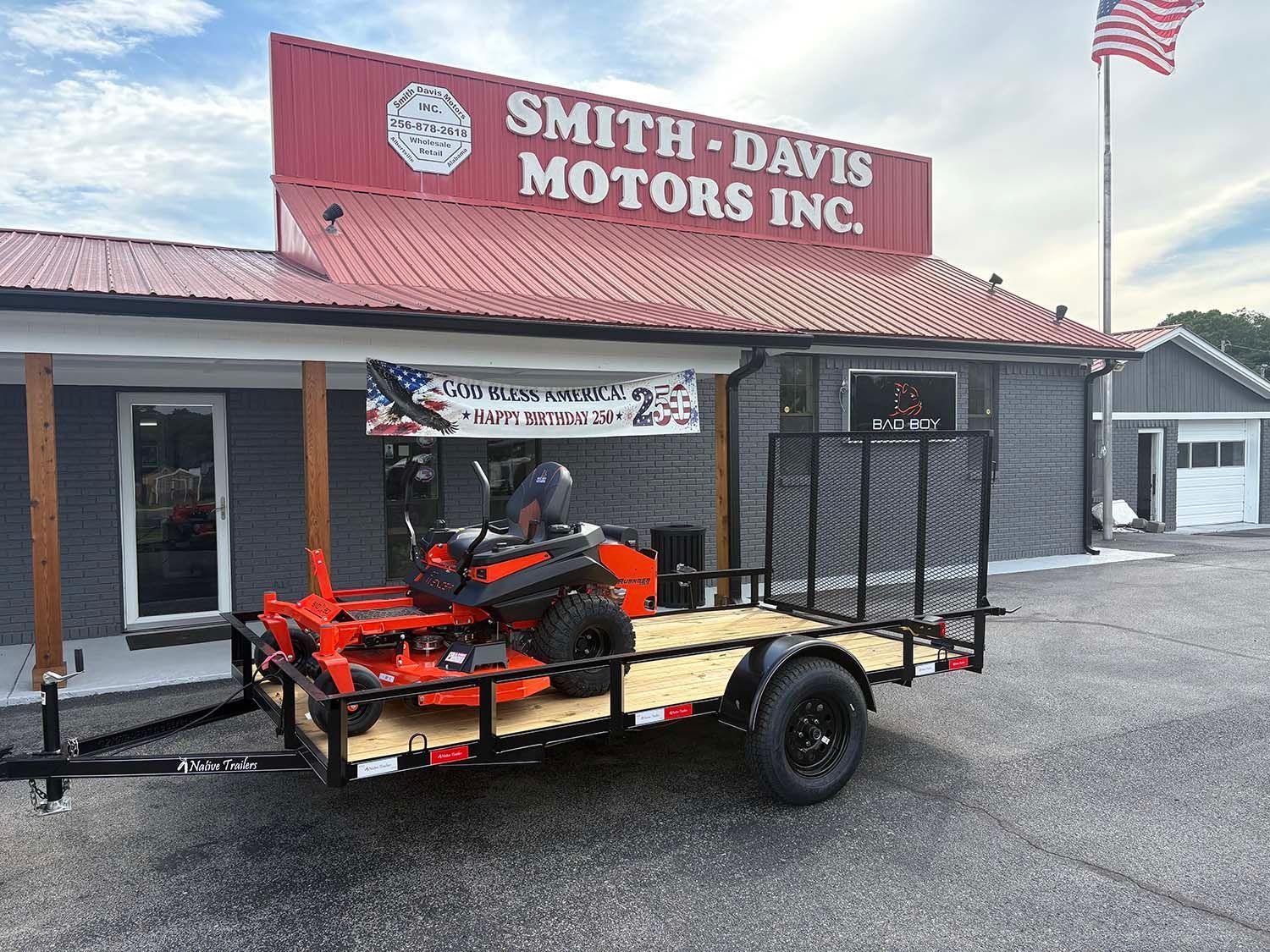 Trailer loaded with a red zero-turn mower parked outside Smith-Davis Motors Inc