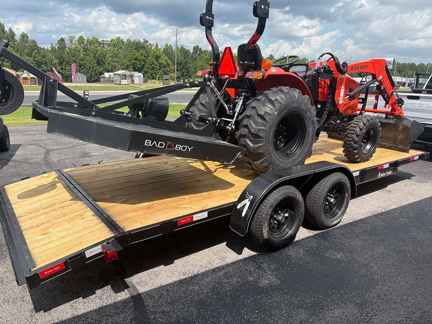 Red tractor on a black flatbed trailer in a parking lot, with another red tractor behind it