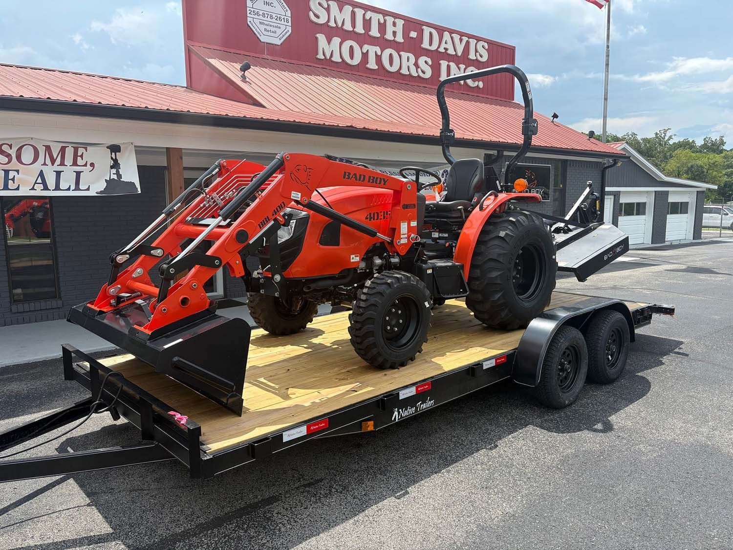 Red tractor and orange loader on a black trailer outside Smith-Davis Motors showroom