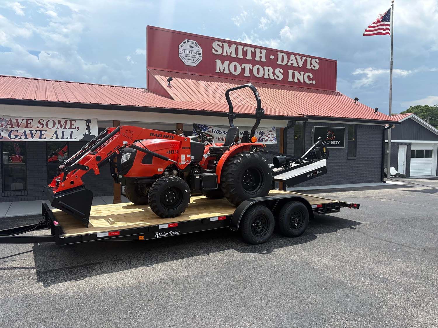 Red tractor on a flatbed trailer outside Smith-Davis Motors Inc. under a cloudy sky
