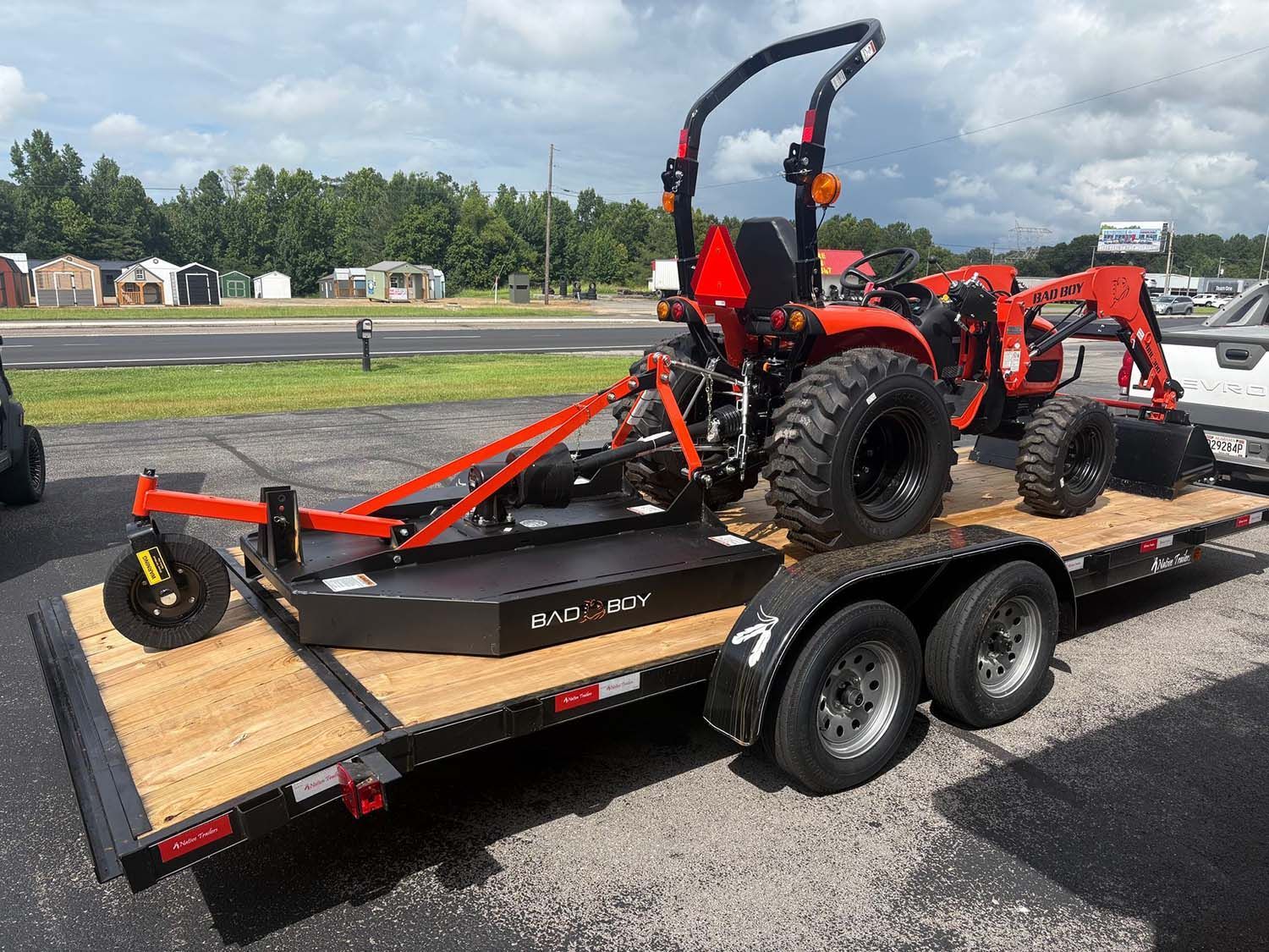 Orange tractor on a flatbed trailer parked outdoors near a road on a cloudy day