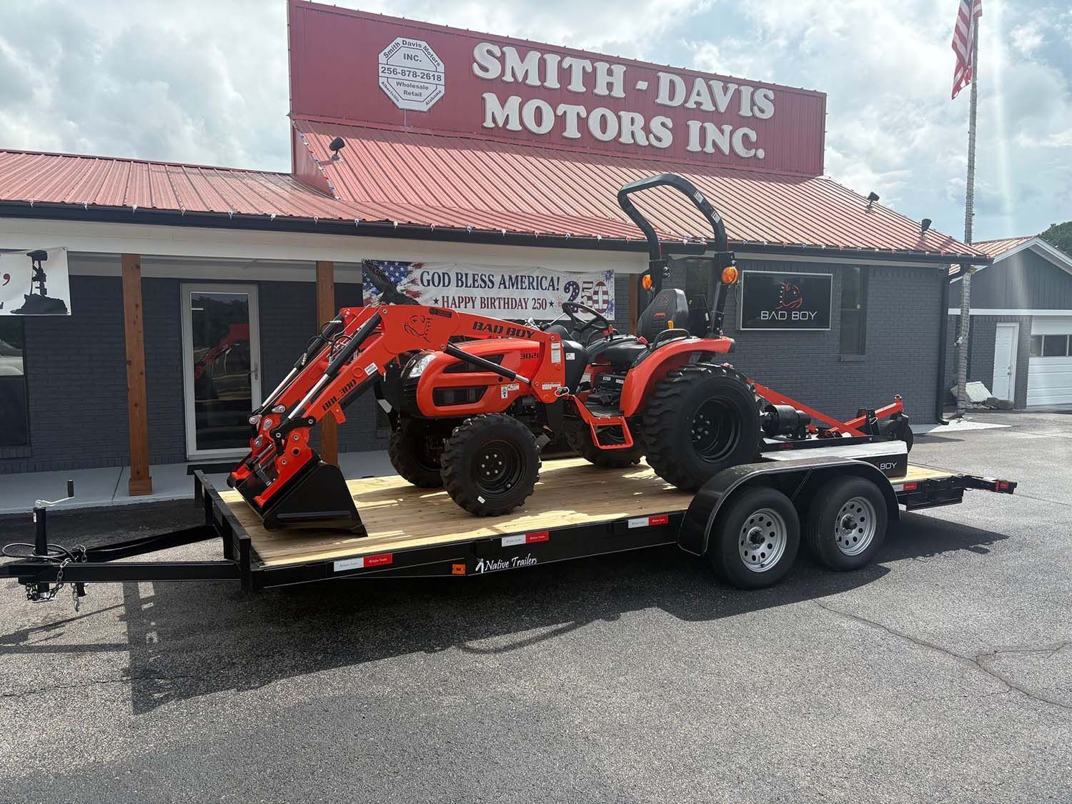 Orange tractor on a flatbed trailer parked outside Smith-Davis Motors Inc
